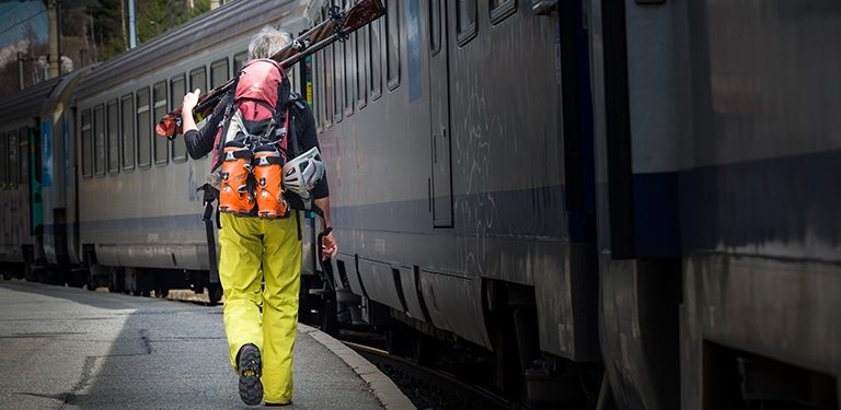 Homme avec des ski sur l'épaule qui va prendre le train. Cette image illustre la campagne Changer d'Approche de Mountain Wilderness France.